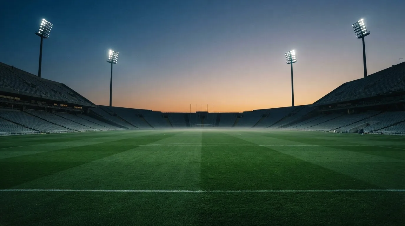 An empty football stadium with floodlight masts at dusk