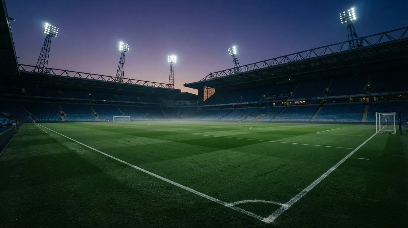 An empty football stadium with floodlight masts at dusk