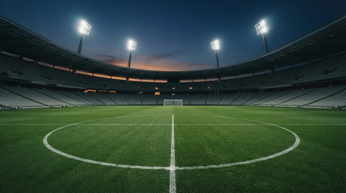 An empty football stadium with floodlight masts at dusk