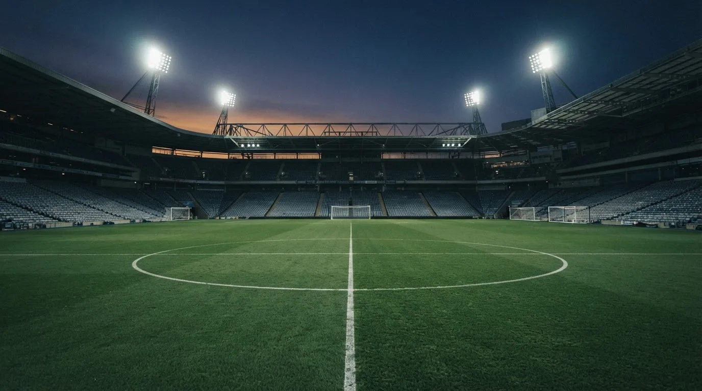 An empty football stadium with floodlight masts at dusk