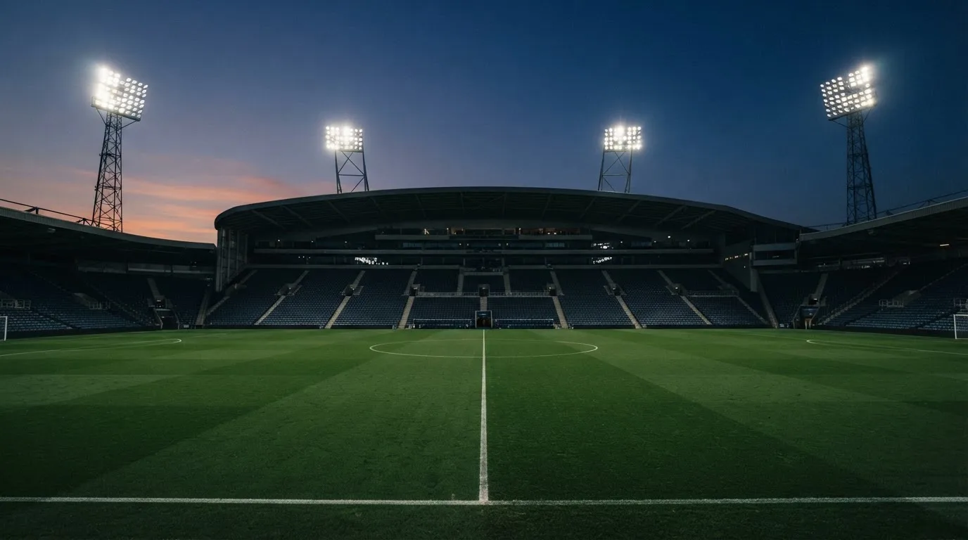 An empty football stadium with floodlight masts at dusk
