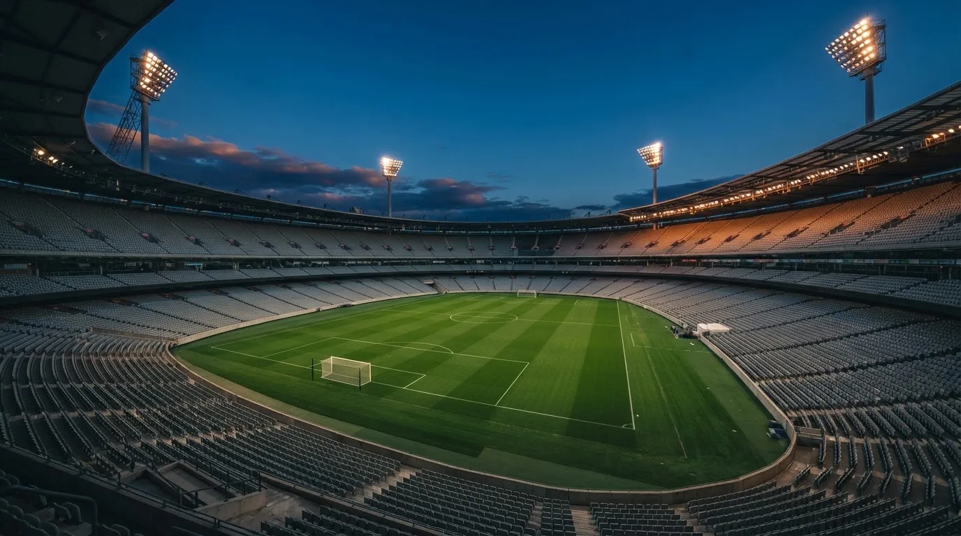 An empty football stadium with floodlight masts at dusk