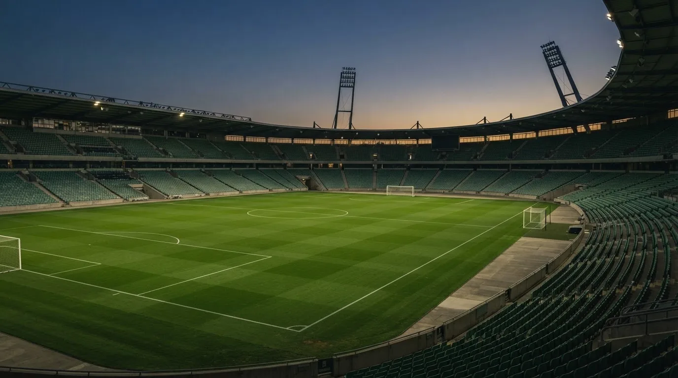 An empty football stadium with floodlight masts at dusk