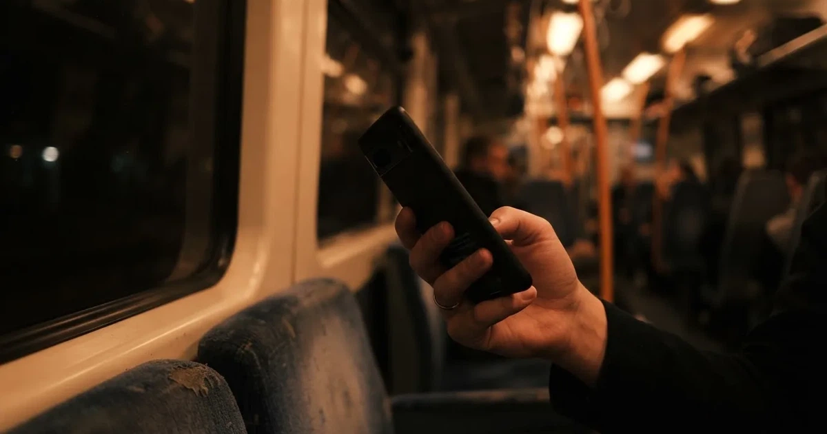 A hand holding a smartphone on a train in the evening, screen turned away