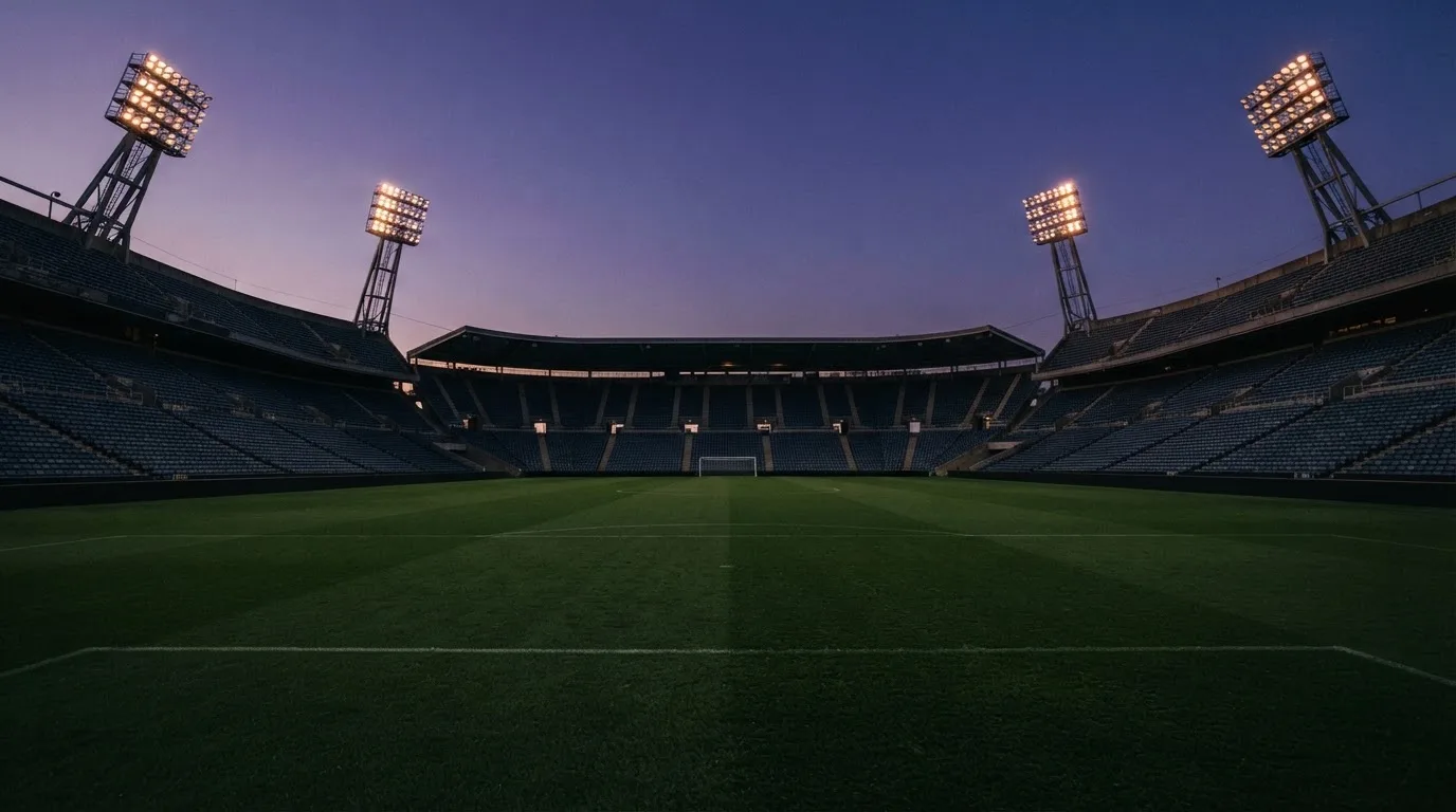 An empty football stadium with floodlight masts at dusk
