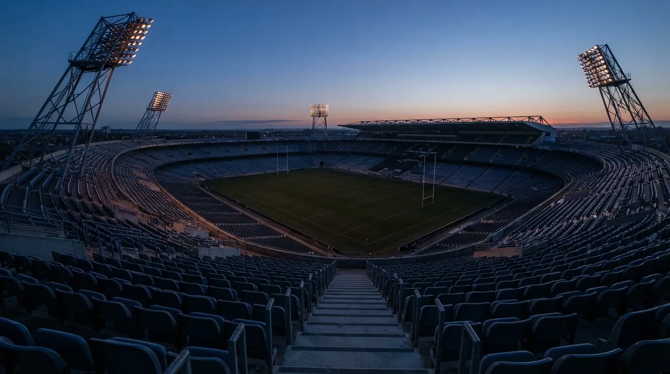 An empty football stadium with floodlight masts at dusk